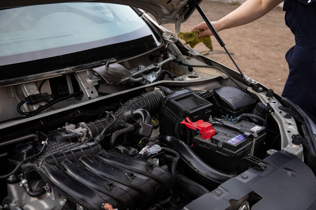 Mechanic inspecting car engine bay and battery during routine maintenance.